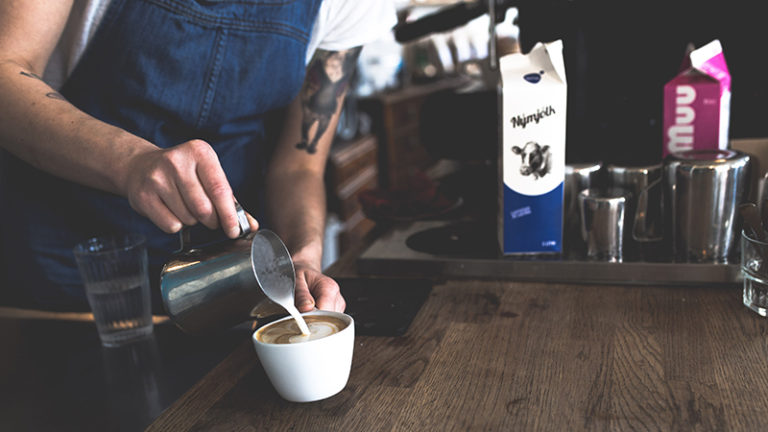 Barista pours steamed milk into coffee